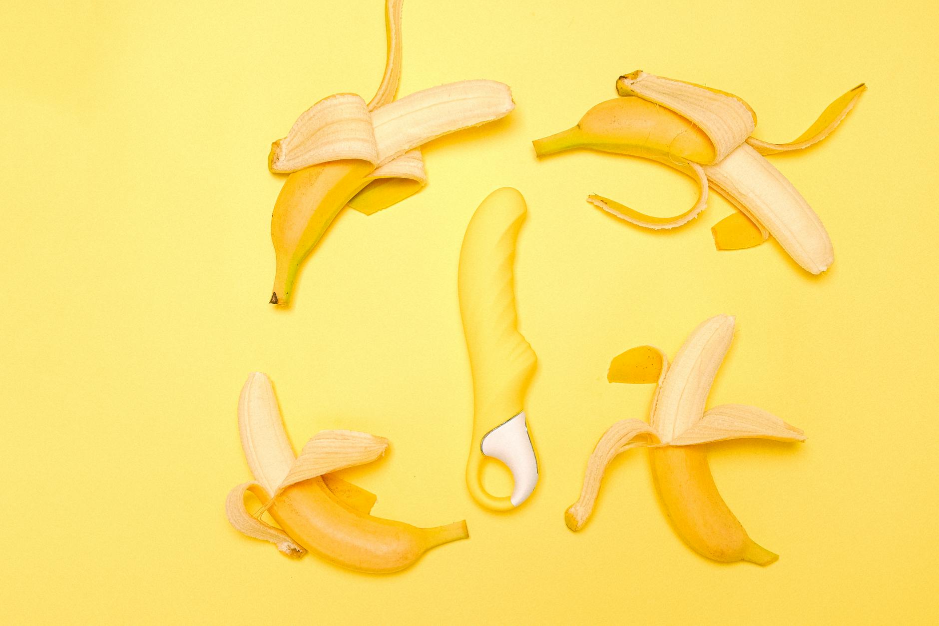 A yellow silicone vibrator surrounded by peeled lemons on a bright yellow background