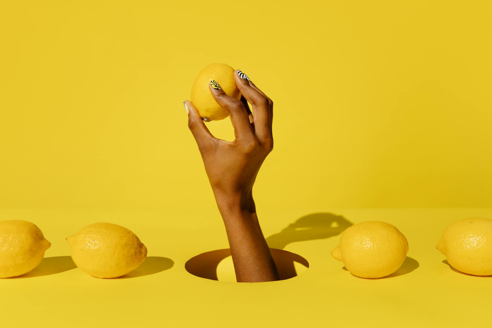 A hand holding a bright yellow lemon against a vivid yellow background, symbolizing fresh sensations and intentional pleasure