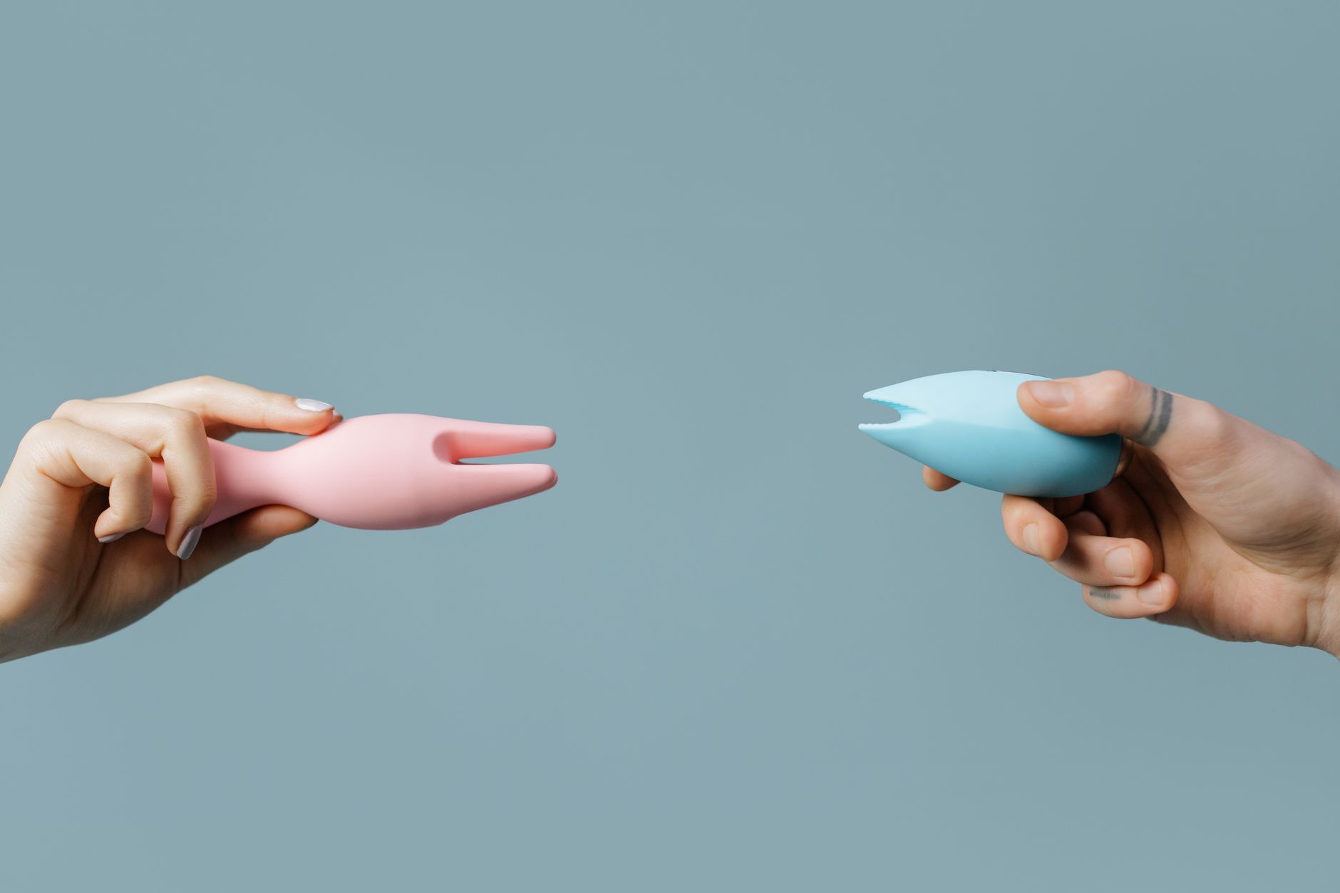 Close-up of hands holding a sleek blue clitoral vibrator against a soft purple background