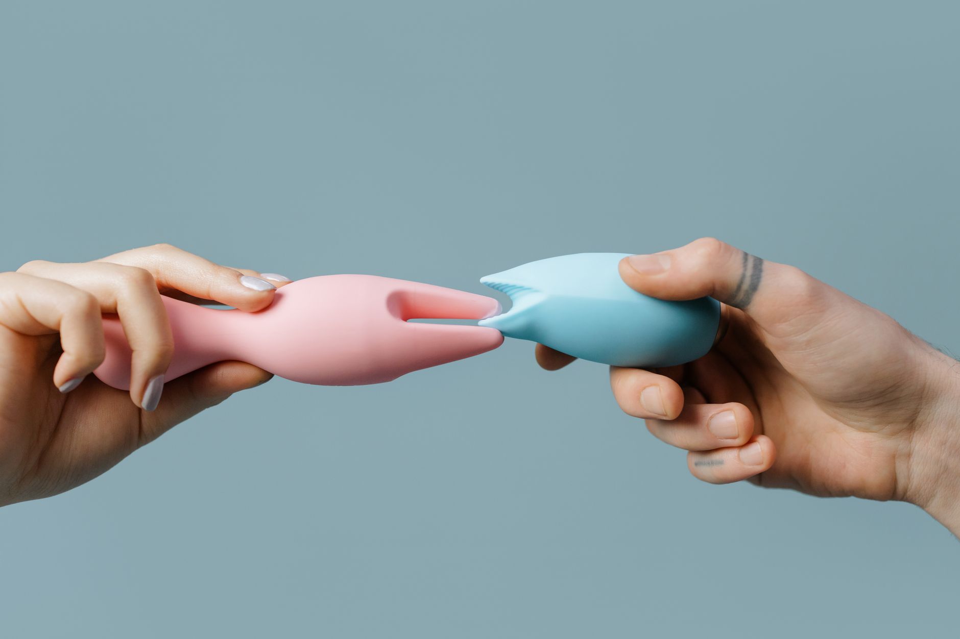 Hands holding colorful silicone vibrators and intimate wellness toys on a neutral surface