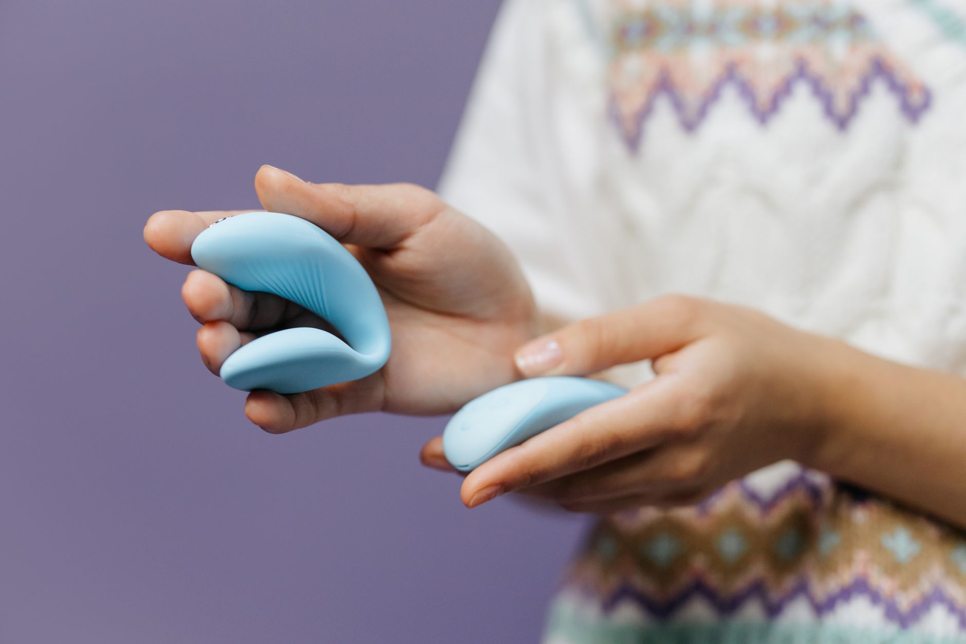 A close-up of hands holding a blue clitoral vibrator against a knitted sweater