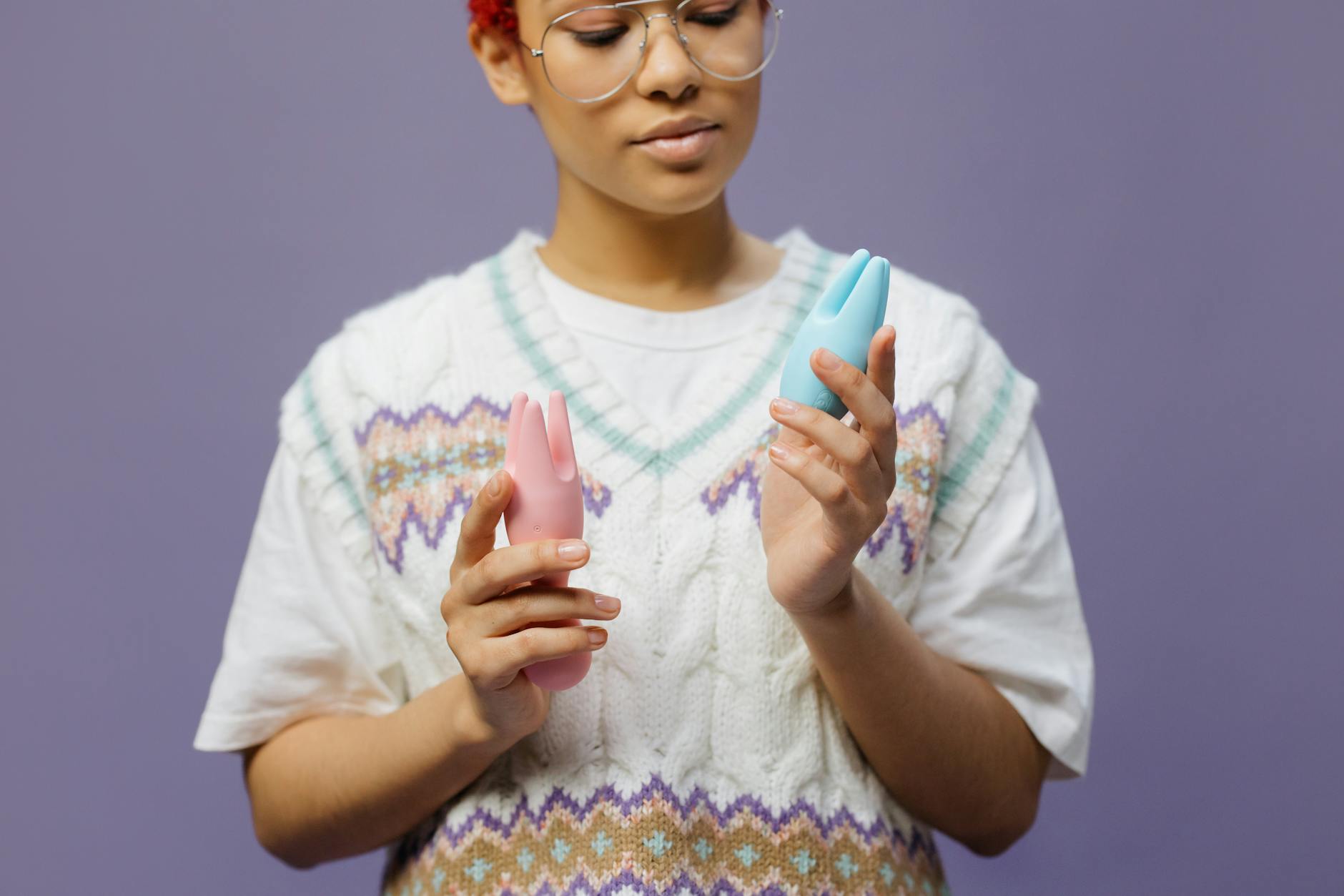 Woman holding blue and pink silicone vibrators in a thoughtful, self-assured moment.